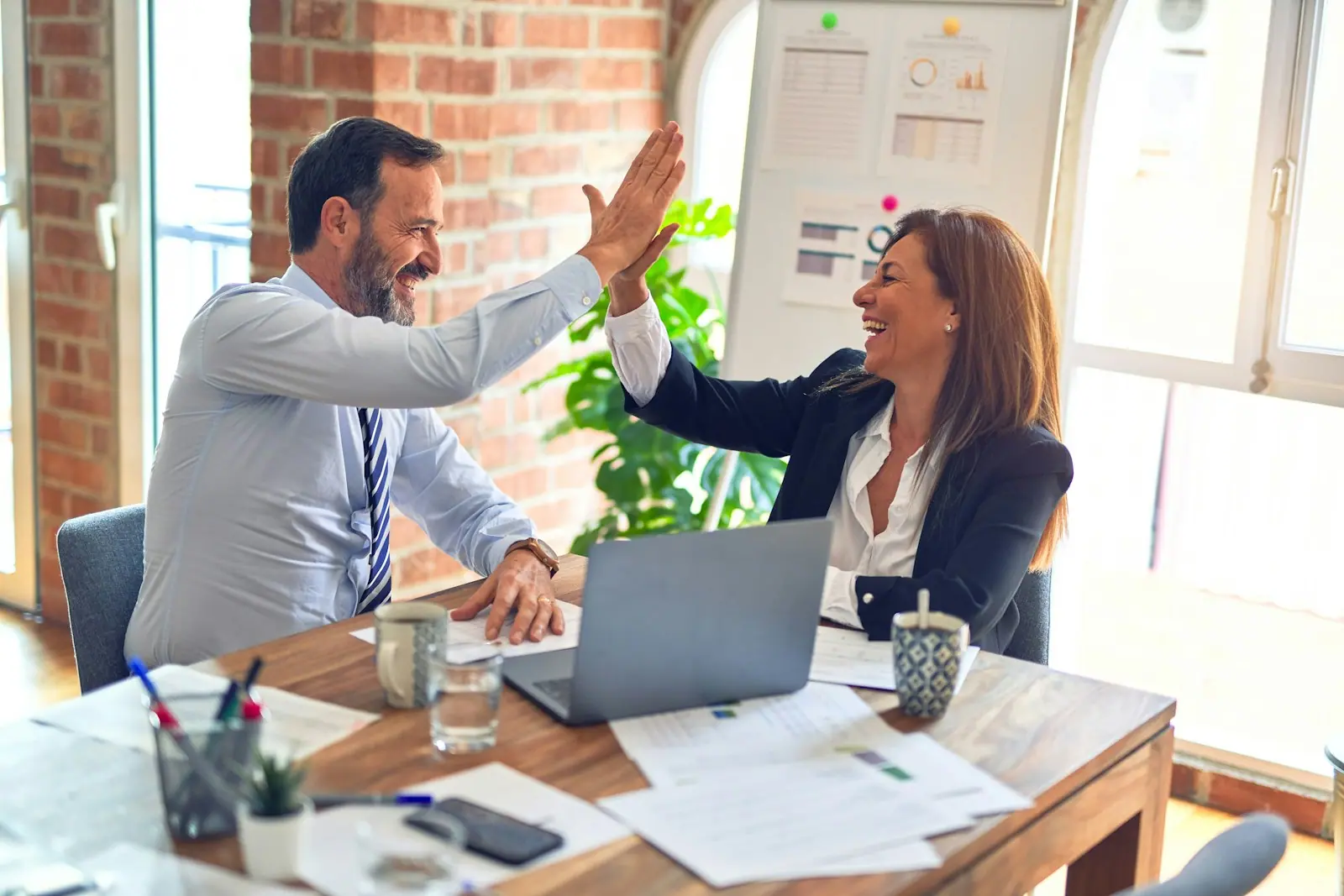 Two colleagues high-fiving at their desk after a win