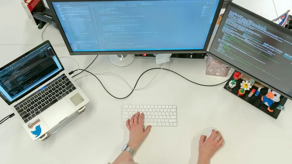 Developer writing code across a laptop and two monitors